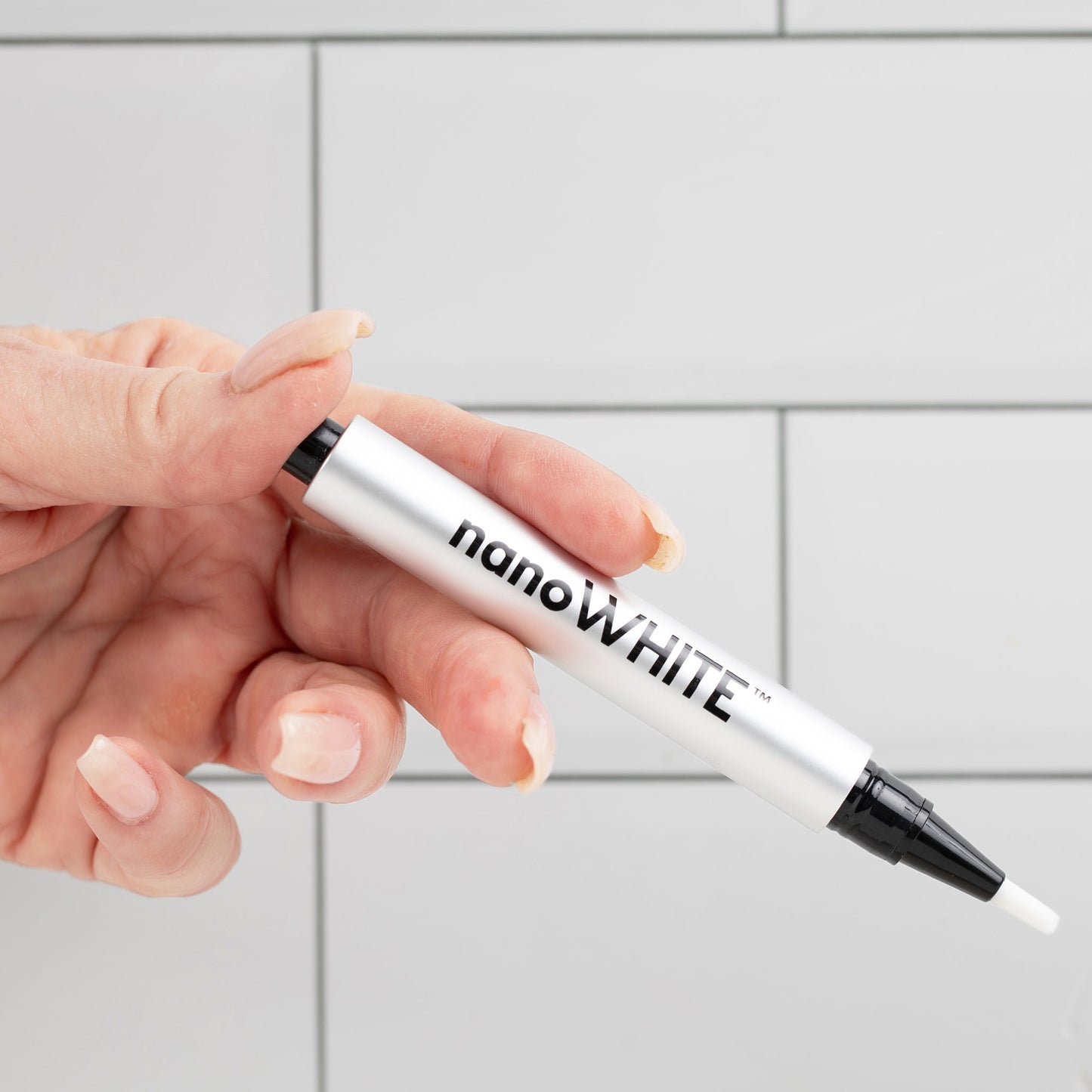 Close-up of nanoWHITE whitening pen fine-tip brush applying gel along teeth and gumline
